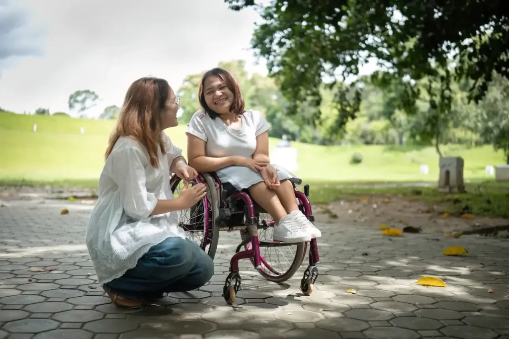 young woman in wheelchair talking to her female support worker who is kneeling beside her.